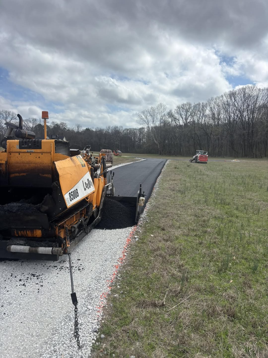 Asphalt paving equipment working along a tree-lined drive